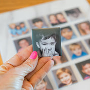 Hand holding a small photo of a child with a blurred background of other children's photos.