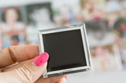 Small black screen device held by a hand with pink nail polish against a blurred background.