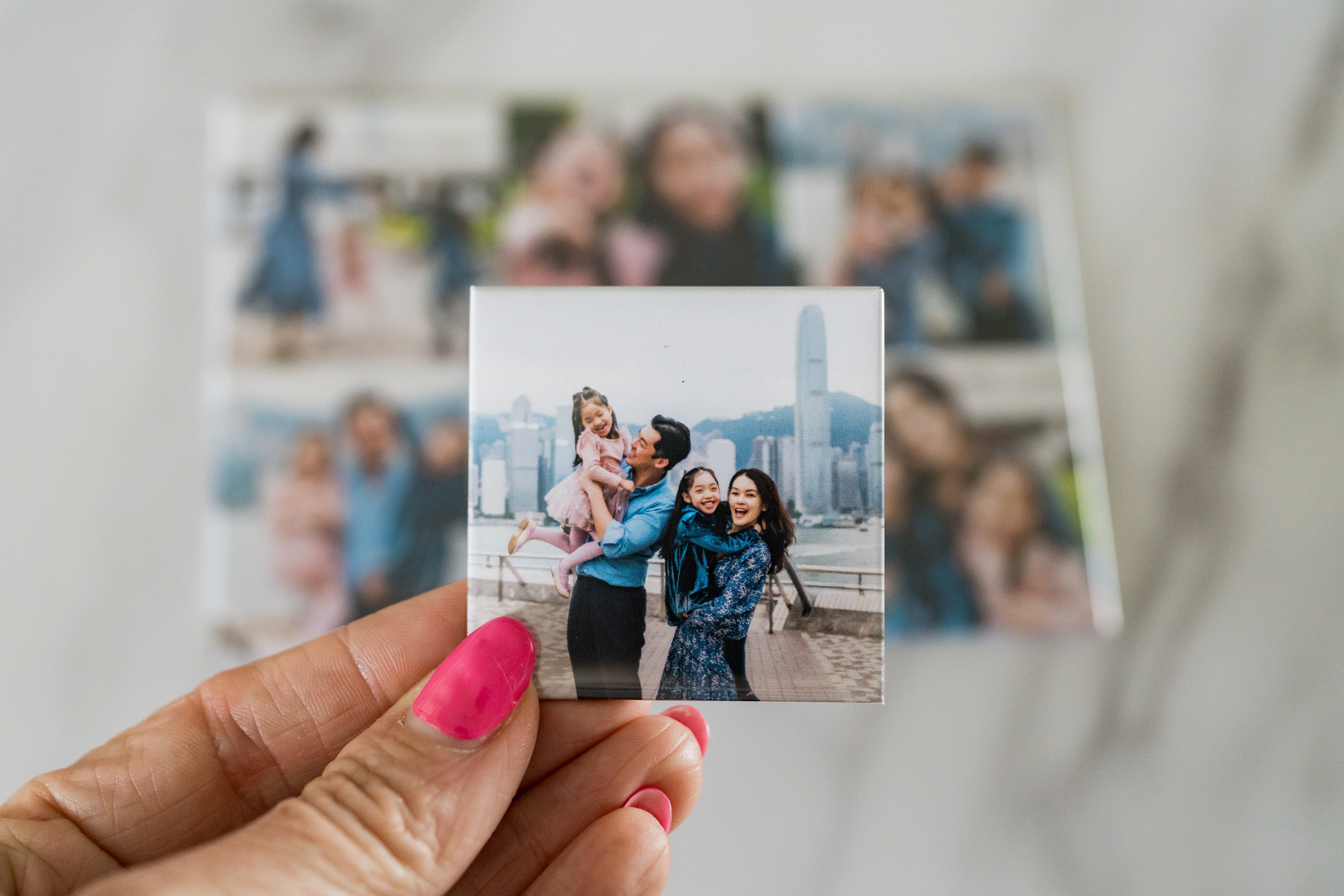Hand holding a small photo print of a family with a cityscape background
